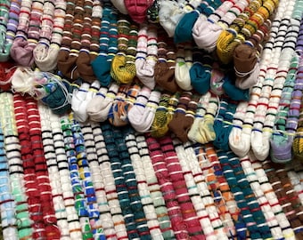 May include: Close-up of a colorful, handmade rag rug. The rug features a variety of colors, including red, white, green, blue, and brown. The texture is created by tightly woven strips of fabric, creating a textured surface.