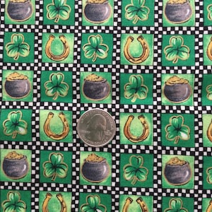 May include: A green and black patterned fabric featuring St. Patrick's Day symbols. The design includes pots of gold, shamrocks, and horseshoes. A U.S. quarter is included for scale.