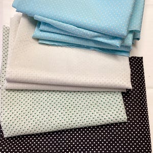 May include: A stack of fabric swatches in various colors, including light blue, white, green, and black. Each fabric features a polka dot pattern. The fabrics are neatly folded and stacked, showcasing the different color options.