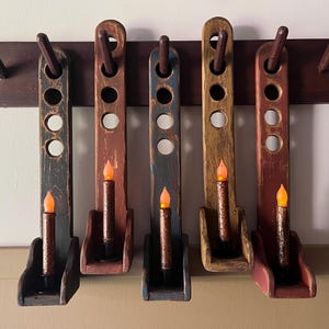 Könnte beinhalten: Fünf Holz-Kerzenleuchter mit einer abgewetzten Lackierung in Rot, Blau und Braun. Jeder Leuchter hat drei Löcher und einen kleinen Kerzenhalter. Die Leuchter sind an einer dunkelbraunen Holzwand befestigt.