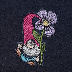 May include: Embroidered patch of a garden gnome with a flower. The gnome has a pink hat, white beard, and blue trousers. The flower is purple with a yellow centre, set against a navy blue background.