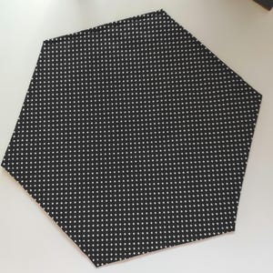 K&ouml;nnte beinhalten: Ein schwarzer, sechseckiger Stoffuntersetzer mit wei&szlig;em Tupfenmuster. Der Untersetzer besteht aus einem weichen Material und sch&uuml;tzt Oberfl&auml;chen vor Hitze und Feuchtigkeit. Das Design ist schlicht und modern.