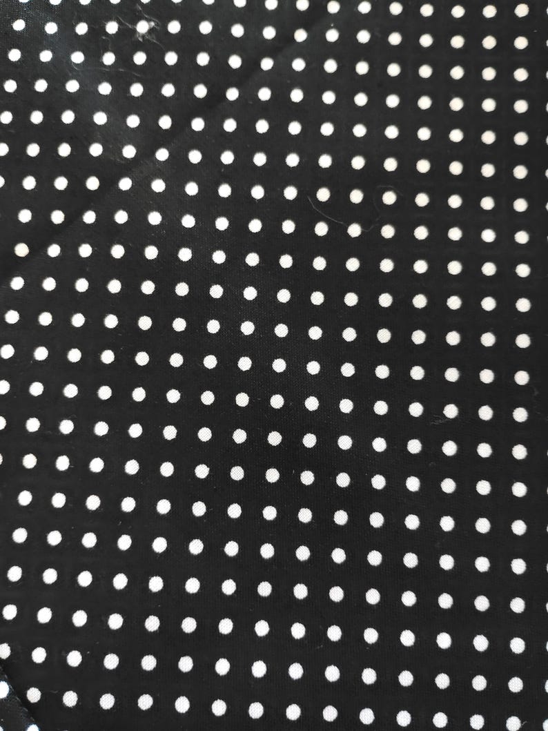 K&ouml;nnte beinhalten: Schwarzer Stoff mit einem sich wiederholenden Muster aus gleichm&auml;&szlig;ig verteilten wei&szlig;en Punkten. Die kleinen, kreisf&ouml;rmigen Punkte erzeugen ein klassisches Design. Dieser Stoff eignet sich f&uuml;r verschiedene N&auml;h- und Bastelprojekte.