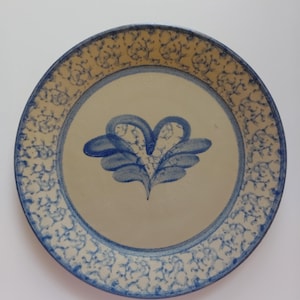 May include: Round ceramic plate with a cream-colored center and a blue floral design. The rim features a blue and tan pattern. A blue floral motif is in the center of the plate.