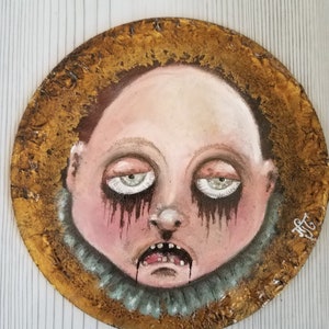 Creepy crying baby face hand painted on round wood piece with textured gold edging