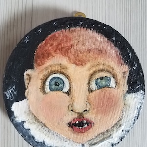 Creepy antique doll face painting on round wood piece with textured edging