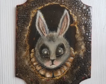 May include: A framed painting of a gray rabbit with large eyes and a ruffled collar. The frame is dark brown with a cracked and distressed finish.