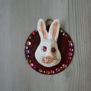 White ceramic rabbit head mounted on round wood edged in faux jewels