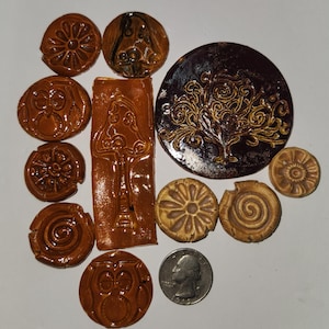 May include: A collection of handmade ceramic pieces in various shapes and designs. The pieces are primarily brown and tan, with embossed patterns including flowers, owls, and a tree. A US quarter is included for size reference. The pieces are likely for crafting or decorative purposes.