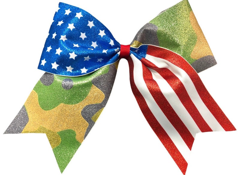 May include: A large glittery bow with a camouflage pattern on one side and an American flag pattern on the other side.
