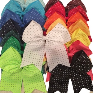 May include: A collection of cheer bows in various colors, each with a white rhinestone design. The bows are arranged in a staggered pattern, with the white bow in the center.
