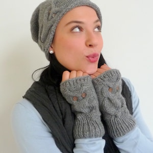 May include: A woman wearing a gray knitted hat and matching fingerless gloves. The gloves have brown buttons.