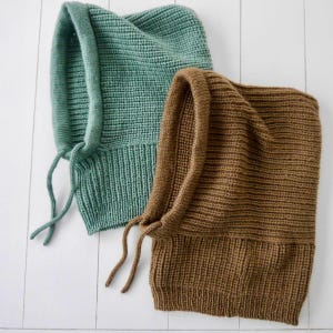 Könnte beinhalten: Zwei gestrickte Sturmhauben in Türkis und Braun. Die Sturmhauben haben einen gerippten Strickbund und eine glatte Strickkapuze. Jede hat einen Kordelzugverschluss. Die Artikel werden auf einer weißen Holzoberfläche präsentiert.