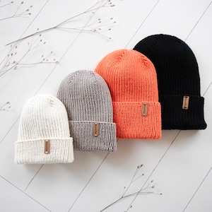 以下が含まれることがあります： 白、ベージュ、オレンジ、黒の4色のニットビーニー。 それぞれのビーニーには、「Woolly」と書かれた小さな茶色の革タグが付いています。