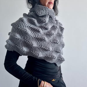 Könnte beinhalten: Ein grauer gestrickter Schal mit Rollkragen und einem strukturierten Muster. Der Schal ist aus weichem, warmem Garn gefertigt und perfekt, um Sie im Winter warm zu halten.