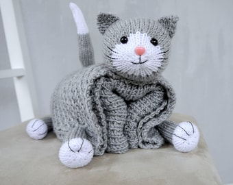 May include: Gray knitted cat tissue box cover with white accents. The cat has a pink nose and black eyes.