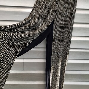 Puede incluir: Pantalones de pierna ancha con estampado blanco y negro y un panel negro en el lateral. Los pantalones están hechos de una tela ligera.