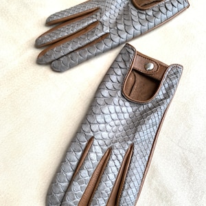 May include: A pair of gray leather gloves with brown leather accents. The gloves have a snakeskin pattern and are made of soft, supple leather.
