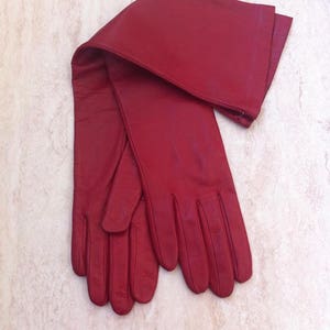 May include: A pair of long red leather gloves. The gloves are folded in half and the fingertips are touching.