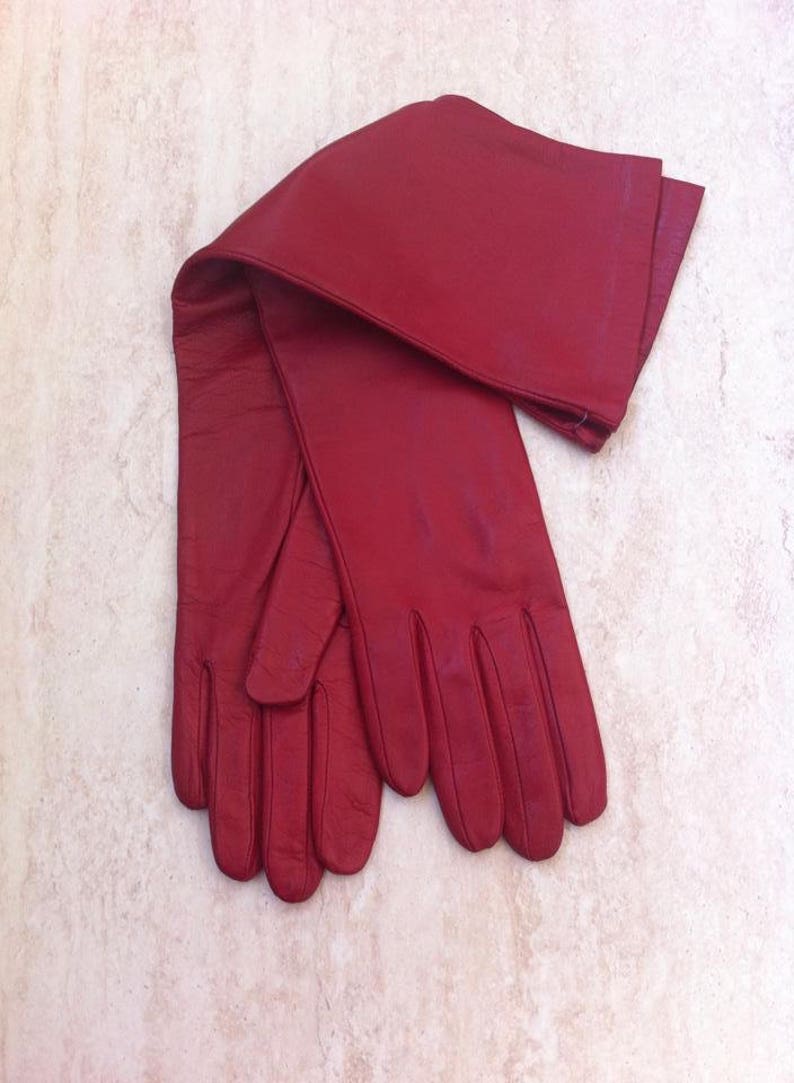 May include: A pair of long red leather gloves. The gloves are folded in half and the fingertips are touching.