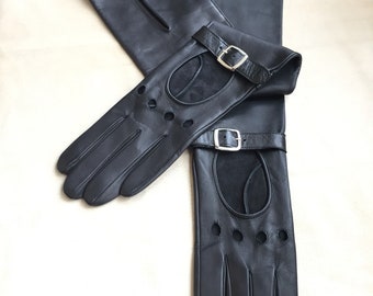 May include: A pair of black leather driving gloves with a suede palm and a buckle closure. The gloves have a perforated design and are long enough to cover the forearm.