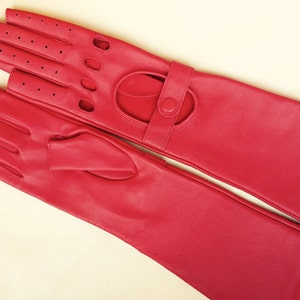 Peut inclure: Une paire de longs gants en cuir rouge avec un design sans doigts et une fermeture &agrave; bouton. Les gants ont un motif perfor&eacute; au dos de la main.
