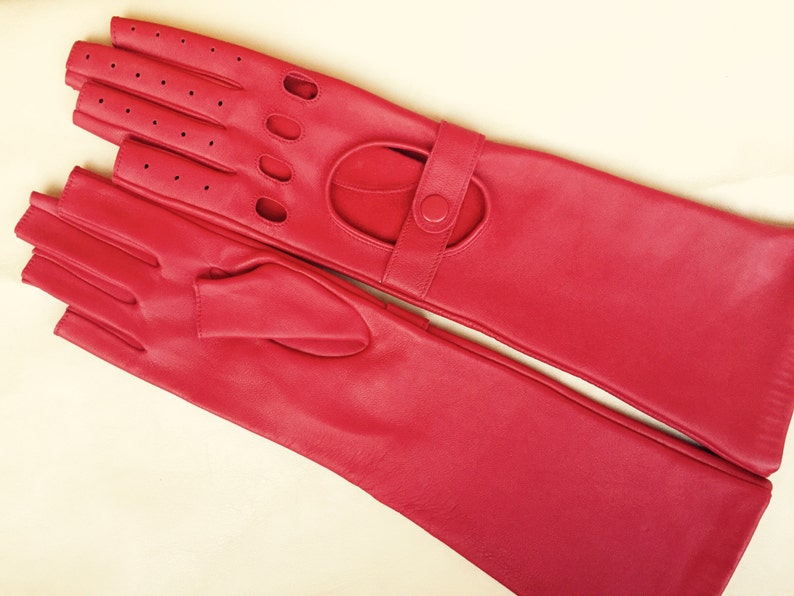 Peut inclure: Une paire de longs gants en cuir rouge avec un design sans doigts et une fermeture &agrave; bouton. Les gants ont un motif perfor&eacute; au dos de la main.