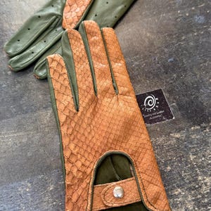 Op de afbeelding: Een paar groene en bruine leren rijhandschoenen met een slangenhuidpatroon. De handschoenen hebben een drukknopsluiting en een klein leren label met de tekst "Sieraden en lederen accessoires".