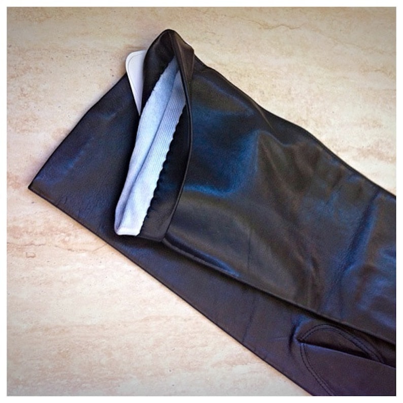 May include: Black leather gloves with a light blue lining. The gloves are long, extending past the wrist. The leather has a slight sheen, and the lining is visible at the opening. The gloves are laid flat on a light-colored surface.
