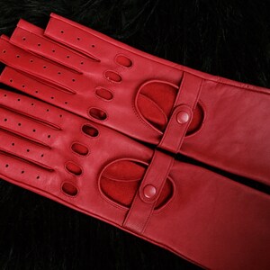 Peut inclure: Une paire de gants de conduite en cuir rouge avec des trous pour les doigts et une fermeture &agrave; bouton sur chaque poignet.