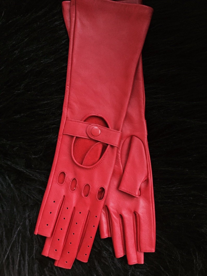 Peut inclure: Une paire de gants de conduite en cuir rouge avec des trous au bout des doigts et une sangle avec une fermeture &agrave; bouton.