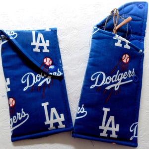 May include: Two blue fabric eyeglass cases with a baseball theme. The cases feature the Los Angeles Dodgers logo, a baseball, and the word "Dodgers" in white script. One case is open, holding a pair of glasses. Each case has a snap closure.