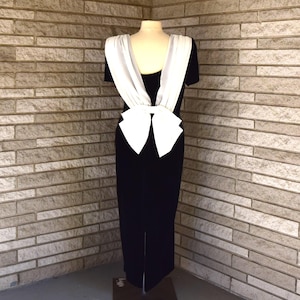 May include: A black velvet dress with a white satin bow on the back. The dress has a scoop neckline and short sleeves.