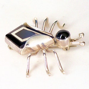 May include: A silver and black onyx brooch in the shape of a stylized spider. The spider has a black onyx body with a silver frame and a black onyx eye.