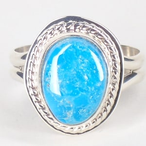 Op de afbeelding: Een zilveren ring met een helderblauwe turquoise steen gezet in een touwachtig ontwerp.
