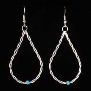 May include: A pair of silver-toned teardrop earrings with a twisted rope design. Each earring features a small, round turquoise bead at the bottom. The earrings hang from a simple hook and are set against a black background.