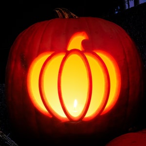 Puede incluir: Dos calabazas talladas con velas encendidas en su interior. La calabaza de la izquierda tiene un diseño de calabaza tallada, mientras que la calabaza de la derecha es lisa. Ambas calabazas son de color naranja y están sobre una superficie oscura.