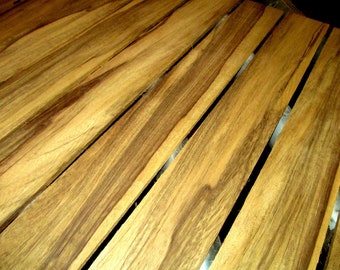 May include: Close-up of several wooden planks with a natural wood grain pattern. The planks are various shades of brown and tan, with darker streaks running through them. The wood appears to be unfinished.
