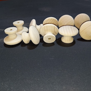 May include: A group of ten unfinished wooden knobs with a brass screw in the center of each knob. The knobs are arranged in a semi-circle on a black surface.
