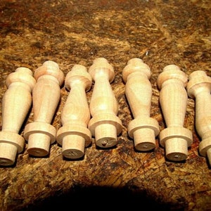 May include: Seven unfinished wooden furniture legs, each with a turned design featuring a bulbous center and a cylindrical base and top. The legs are made of light-colored wood and are arranged on a brown surface.