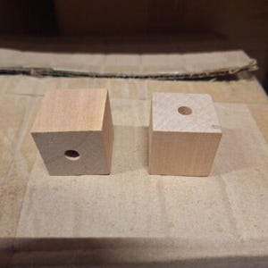 May include: Two unfinished wooden blocks with a hole drilled in the center of each block.