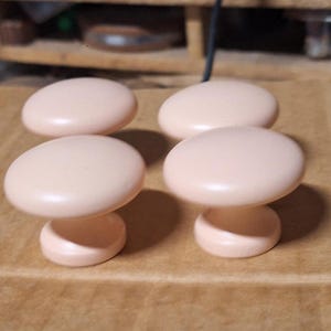 May include: Four small, pale pink ceramic knobs with a rounded top and a short, cylindrical base.
