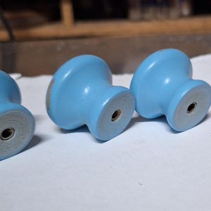 May include: Three light blue wooden cabinet knobs with a silver screw in the center of each knob.