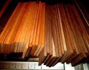May include: A collection of wooden planks in varying shades of brown and orange. The planks are stacked and arranged, showcasing the natural wood grain. A metal ruler is visible at the bottom, indicating measurements.