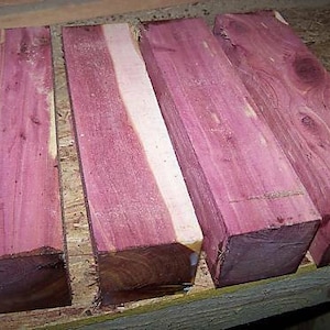 May include: Four pieces of purple heart wood, each approximately 12 inches long and 2 inches wide. The wood has a beautiful purple and white grain pattern.
