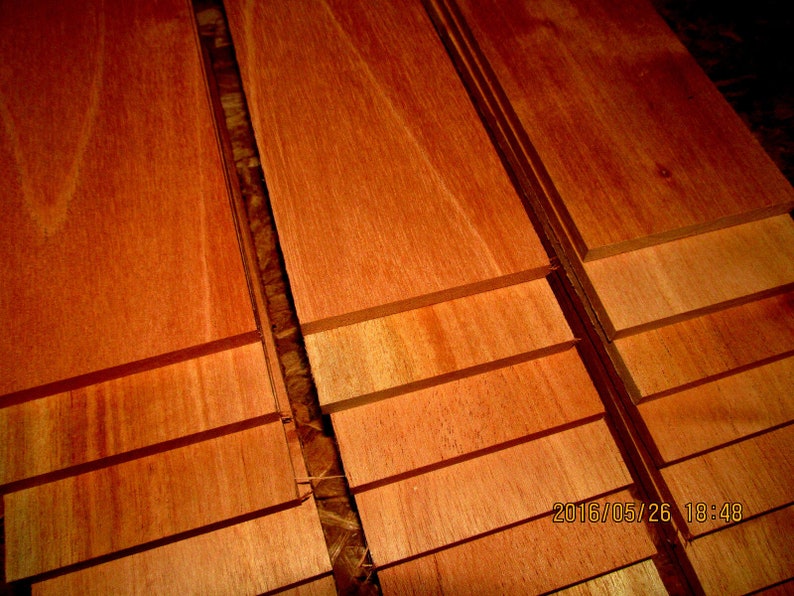 May include: Stacked wooden boards in various shades of reddish-brown, showing the natural grain of the wood. The boards are arranged in a staggered pattern, creating a visual texture.