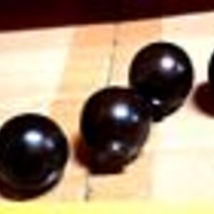 May include: Five black bowling balls lined up on a wooden surface.
