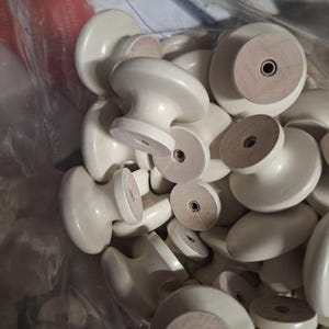 May include: A bag of white ceramic cabinet knobs with a wood base. The knobs have a simple, round design.