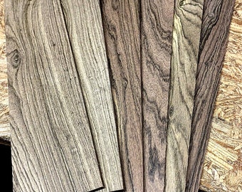 Puede incluir: Un conjunto de ocho tiras de chapa de madera en varios tonos de marrón y gris. Las tiras tienen un patrón de veta de madera natural y están dispuestas en forma de abanico.