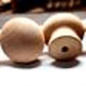 May include: Four wooden knobs with a smooth, rounded top and a slightly raised base. The knobs are a light brown color and have a natural wood finish.